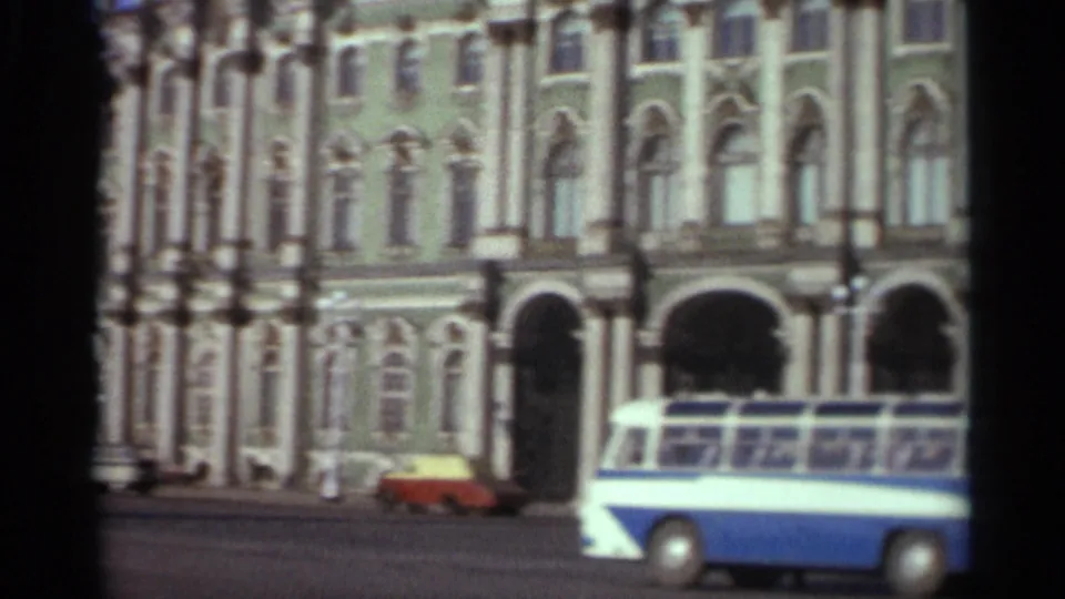 1965 Leningrad 8mm frame showing a blue-and-white bus passing the ornate green building.