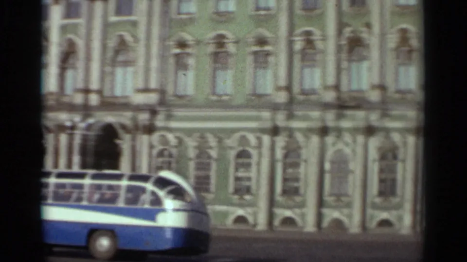 1965 Leningrad frame with a blue-and-white bus moving past arched windows on the green building.