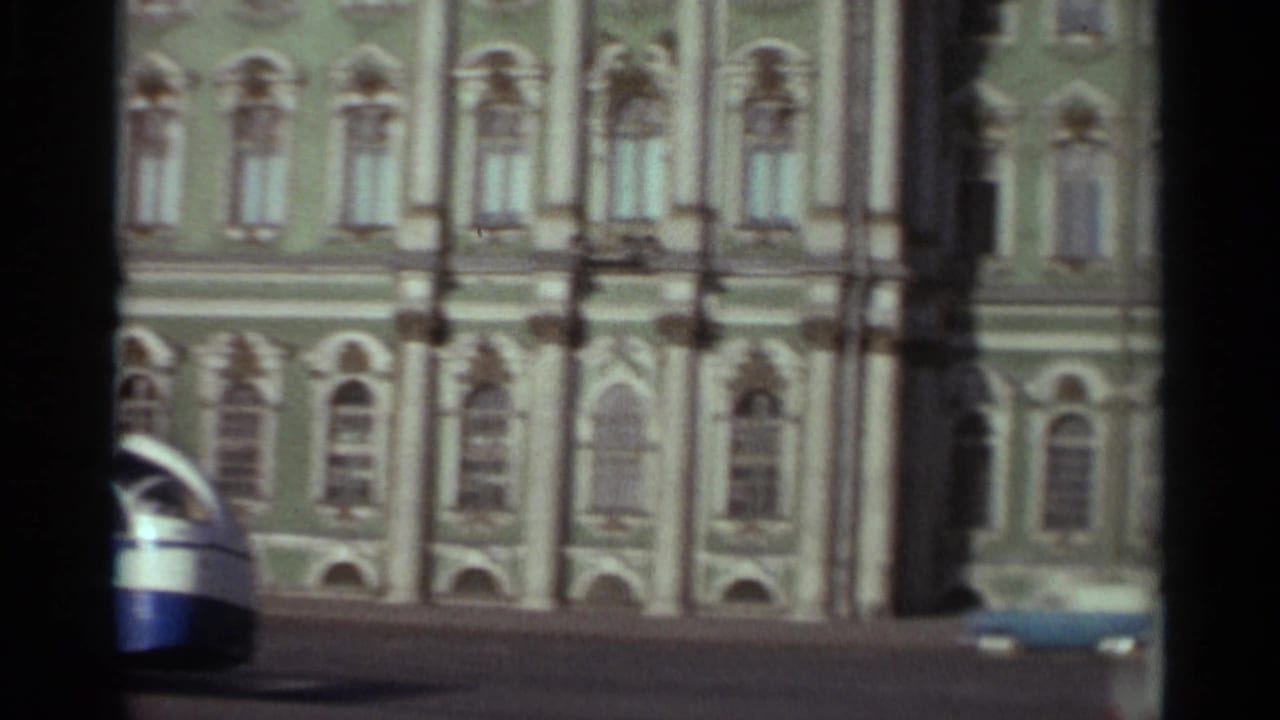 1965 Leningrad waterfront view with ornate building facade, passing vehicles, and heavy 8mm frame borders.