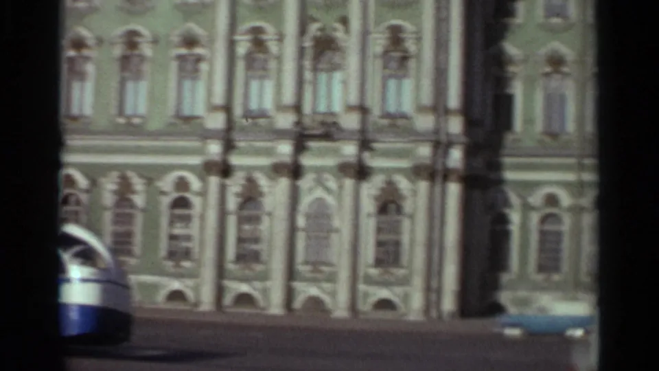 1965 Leningrad waterfront view with ornate building facade, passing vehicles, and heavy 8mm frame borders.