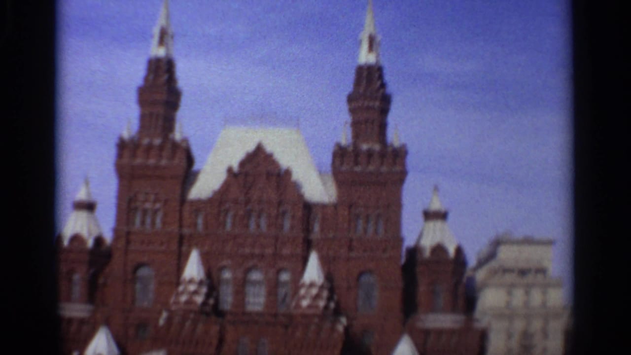 1965 Leningrad frame showing the upper facade of a large brick building with towers, white-capped spires, and blue sky.