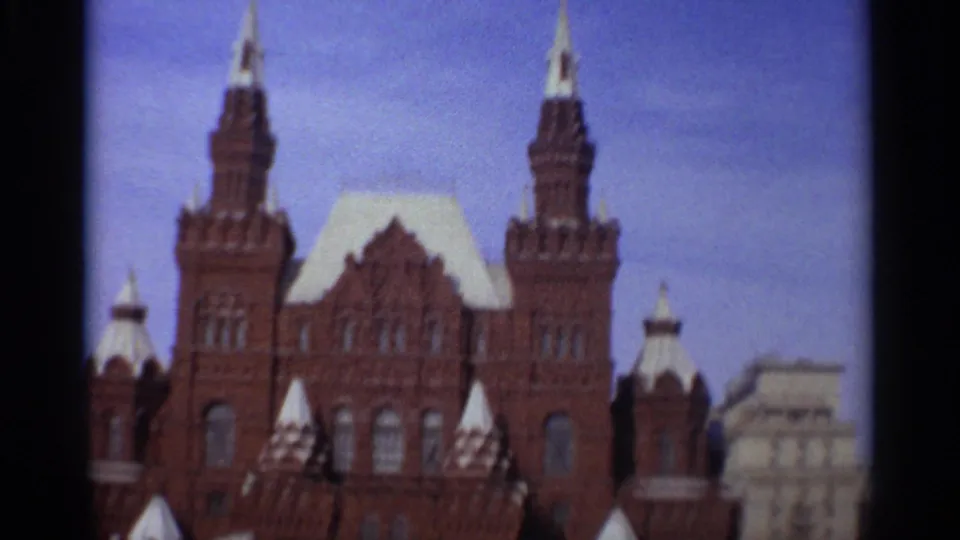 1965 Leningrad frame showing the upper facade of a large brick building with towers, white-capped spires, and blue sky.