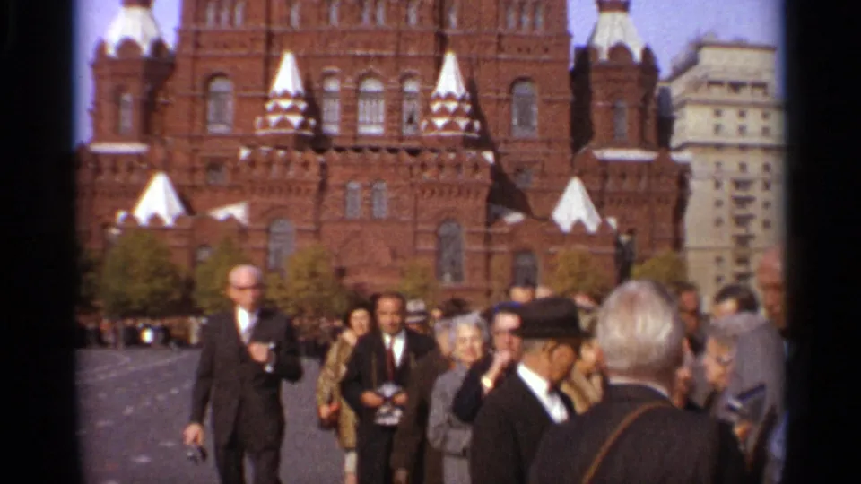 1965 Leningrad street view with adults in suits, hats, and coats moving in front of a large brick building with white spires.