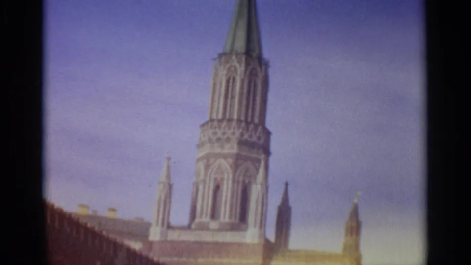 A historic red-brick tower and wall fill the frame, with soft-focus 8mm color and clear sky behind.