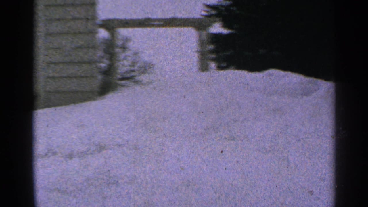 1965 Minnesota 8mm frame showing deep snowbanks outside a building, viewed through a dark interior frame.