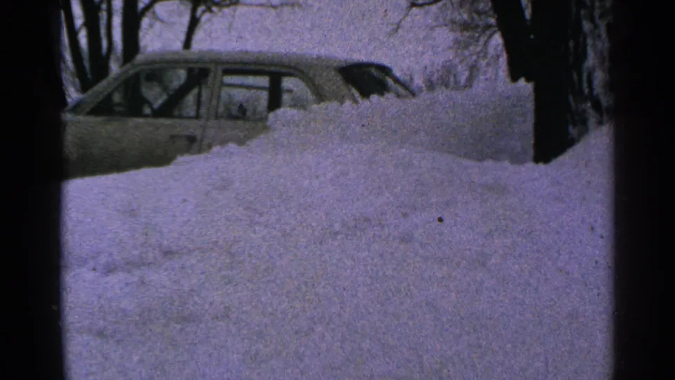1965 Minnesota 8mm view of a light sedan nearly blocked by piled snow in a wintry yard.