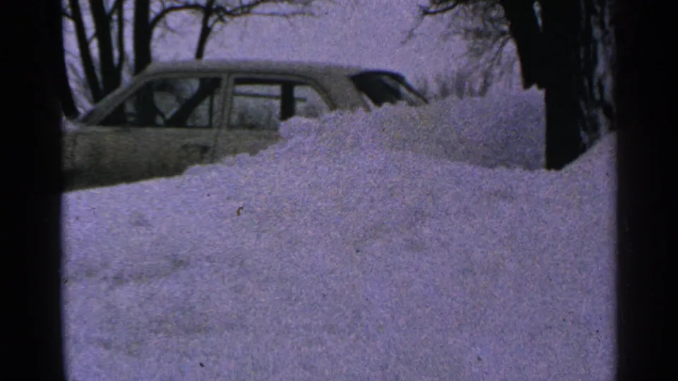 1965 Minnesota winter home-movie frame showing a sedan behind a snowbank in a residential yard.