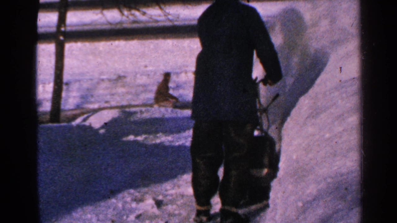 Bundled man stands behind a snow-clearing machine beside a high snowbank.