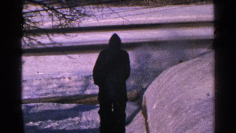 A man in dark winter clothing is seen from behind in a snowy Minnesota setting, framed by bare branches and a fence.