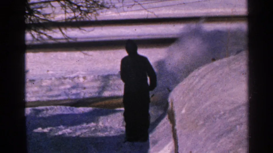 1965 Minnesota 8mm frame showing the man shifted along the snowy walkway, with blown snow visible beside the snowbank.