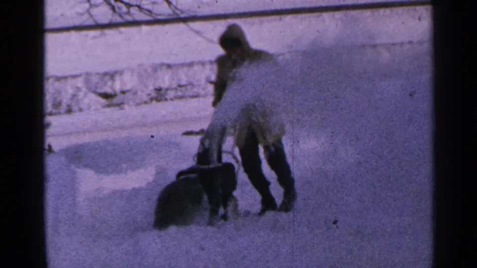 1965 Minnesota frame of a bundled man operating a small snow blower, throwing snow to one side.