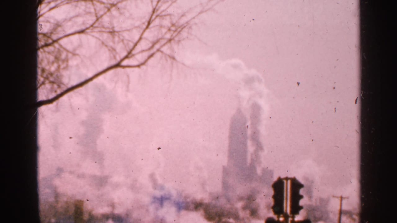 Industrial smoke fills the skyline behind a foreground traffic signal and roadside poles.