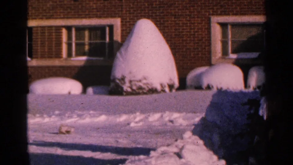 The final 1965 Minnesota frame holds on snowbanks, brick windows, and rounded shrubs under cold winter light.