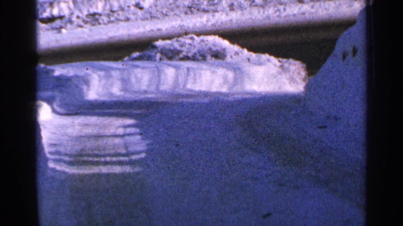 Snow-covered road edge and high snowbank seen through dark film borders.