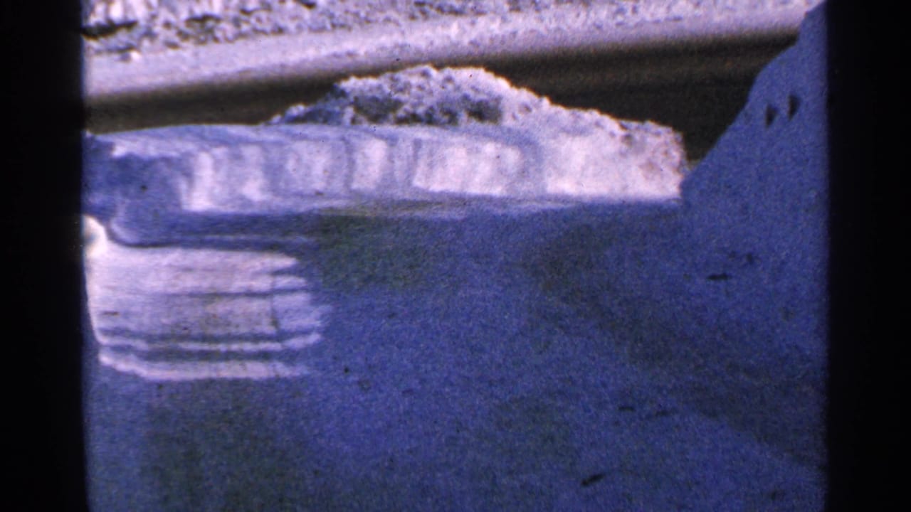Blue-tinted 8mm view of a snowy Minnesota road surface and plowed snowbank, framed tightly by the film gate.