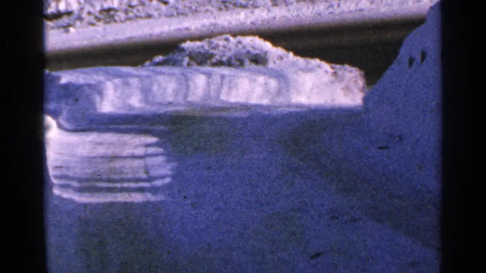 Blue-tinted 8mm view of a snowy Minnesota road surface and plowed snowbank, framed tightly by the film gate.