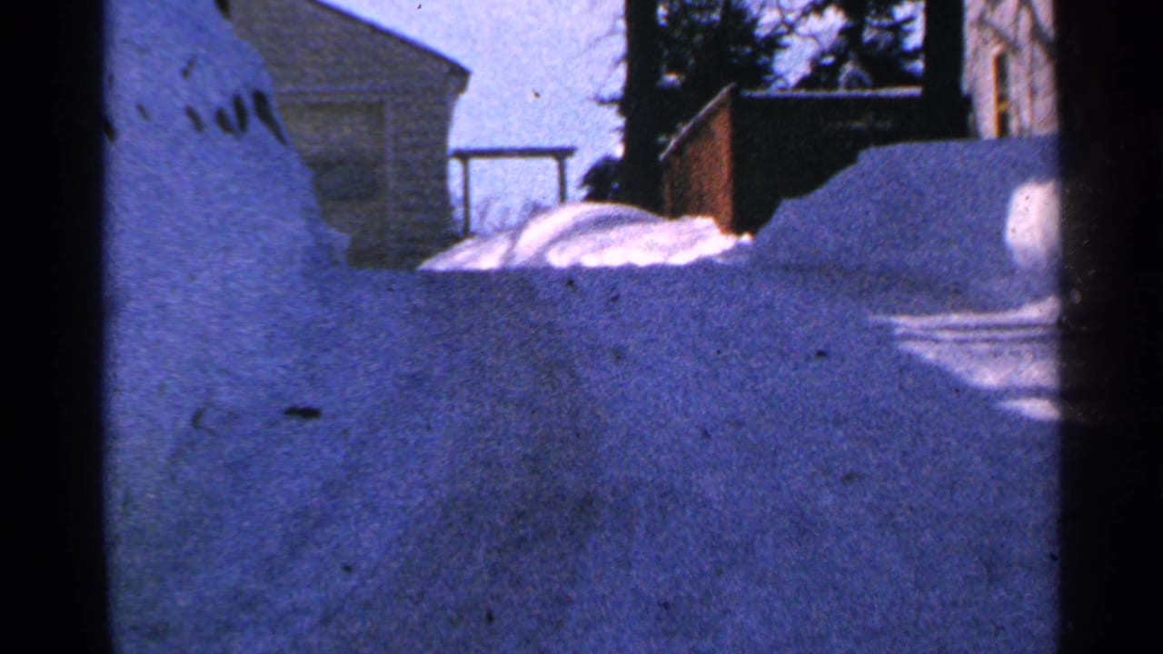 Deep snowbanks beside a residential house and trees in winter light.