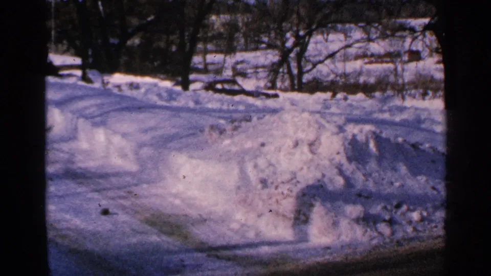 1965 Minnesota 8mm view of a snow-covered rural roadside with plowed banks and bare trees in the distance.