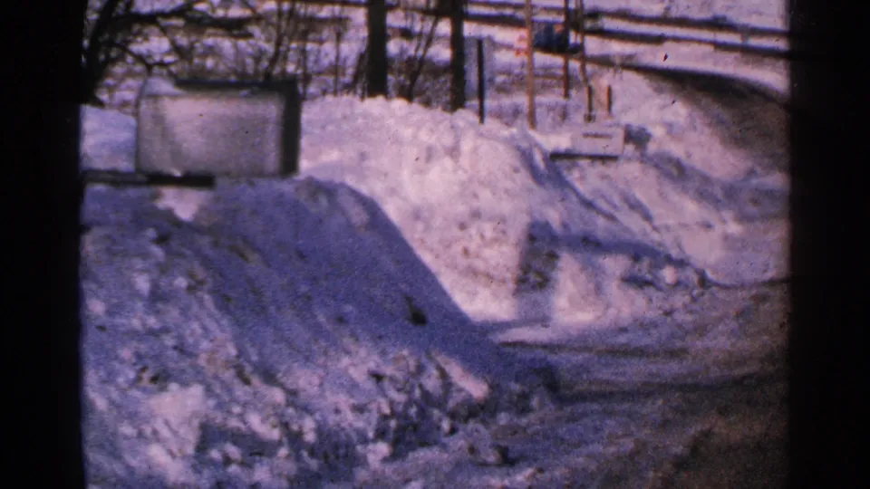 1965 Minnesota frame showing a roadside mailbox, fence posts, packed snowbanks, and a plowed winter road.