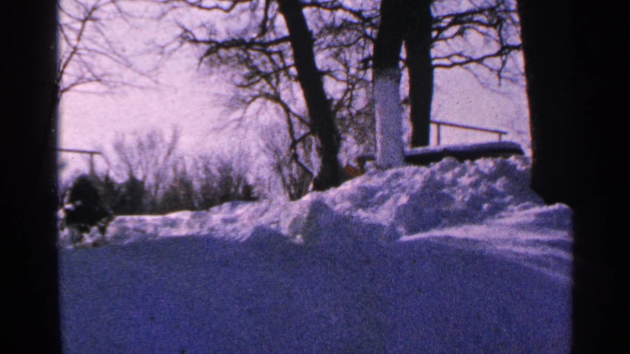 1965 Minnesota 8mm frame showing cleared pavement, piled snow, bare trees, and a pale winter sky.