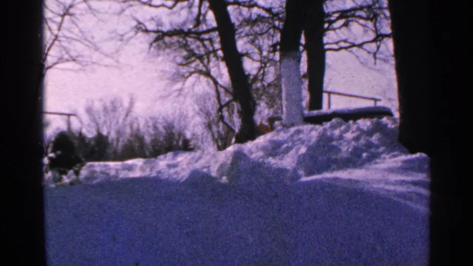 1965 Minnesota 8mm frame showing cleared pavement, piled snow, bare trees, and a pale winter sky.