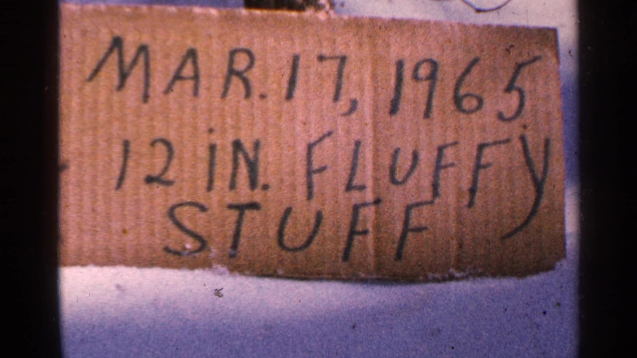 Handwritten cardboard sign in snow reads Mar. 17, 1965 and 12 in. fluffy stuff, in color 8mm footage from Minnesota.