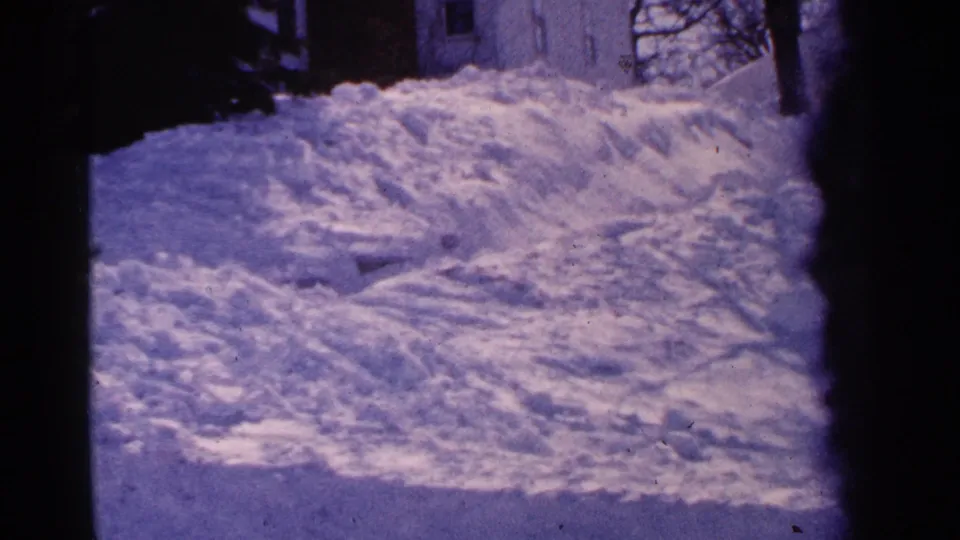 1965 Minnesota 8mm frame showing a snow-covered residential yard area with a house edge and dark film borders.