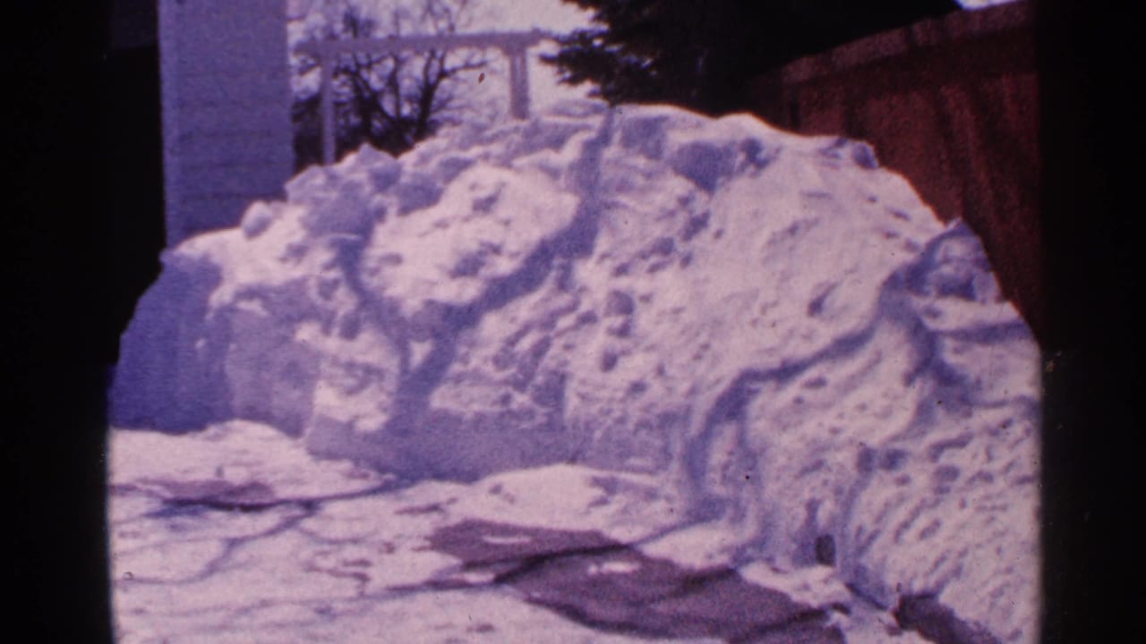 Snowbank beside a wooden fence in a snow-covered residential yard.