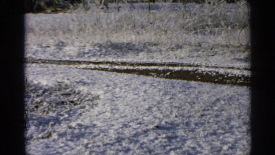 1965 Minnesota 8mm frame showing open snow-covered ground bordered by a dark curve of water, ice, or exposed earth.