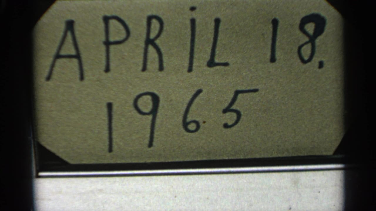 1965 8mm frame with a handwritten April 18 date card above a muted, distant water landscape in Minnesota context.