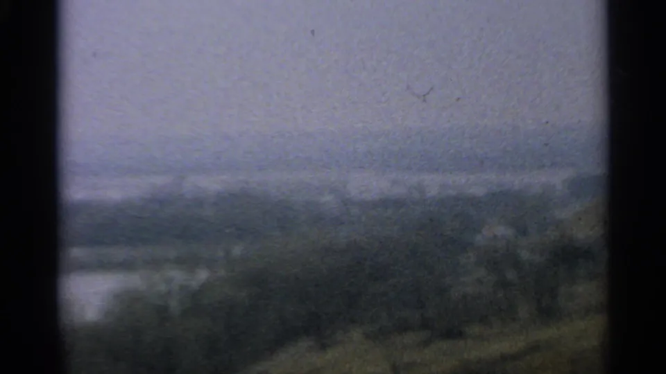 1965 Minnesota 8mm frame showing a soft, overcast river or lake edge with distant forest and visible dark gate borders.