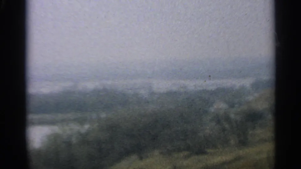 1965 Minnesota home-movie view of a muted river or lake landscape, with soft focus, grain, and a distant wooded bank.