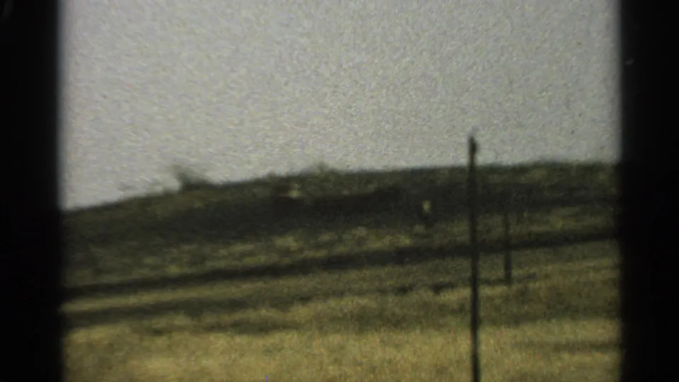 1965 Minnesota 8mm frame showing grassy rolling land and simple fence posts under a bright washed-out sky.
