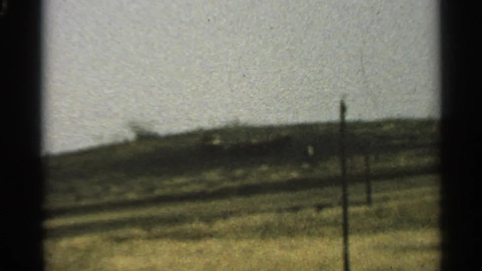 1965 Minnesota home-movie frame of a grassy rural landscape with fence posts and a low, soft horizon.
