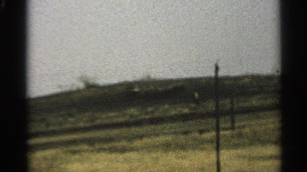 Blurred roadside landscape seen through a dark car-window frame.