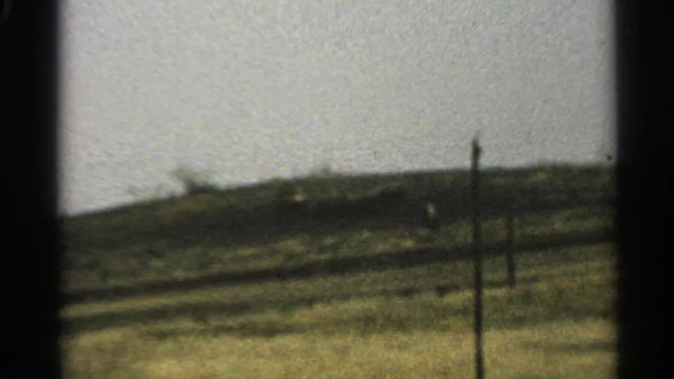 1965 Minnesota 8mm frame showing a soft, distant roadside landscape through a dark car-window edge.