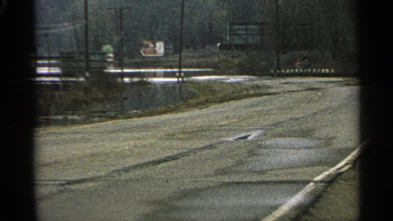 Curving empty road with utility poles, roadside signs, and bare trees.