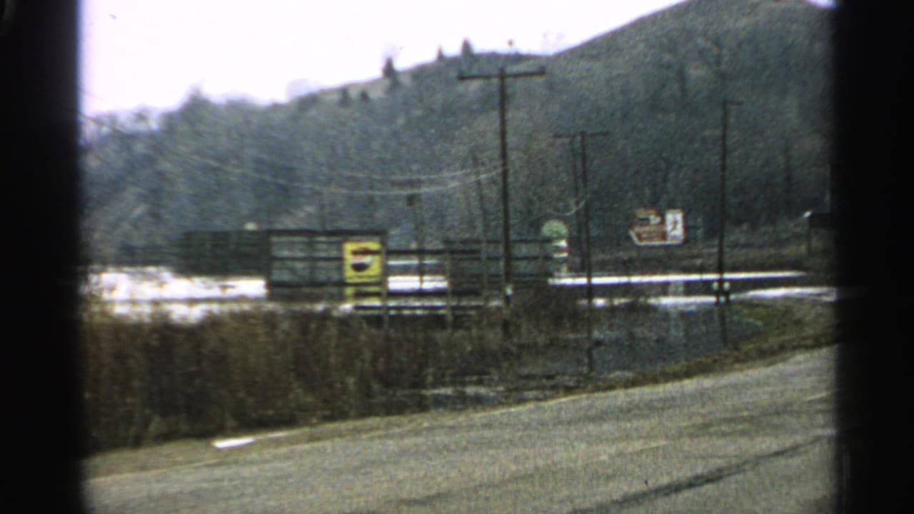 Roadside view with poles, wires, signs, water, brush, and hillside.