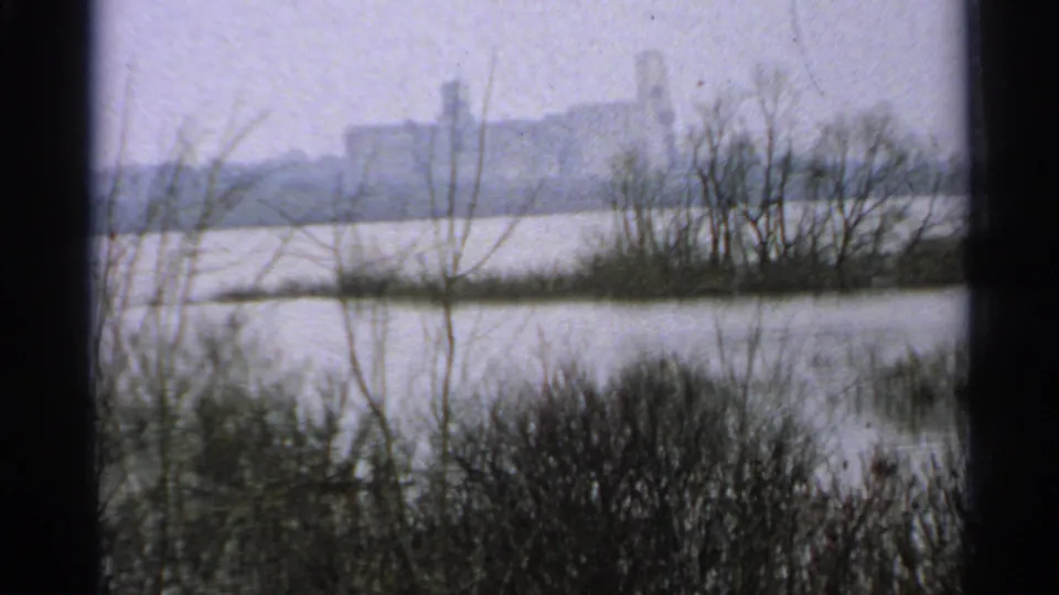 1965 Minnesota home-movie frame showing water and winter-bare trees with a distant building across the far bank.