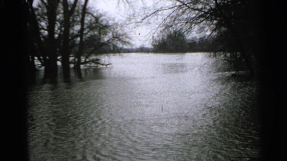 1965 Minnesota 8mm frame showing high floodwater around leafless trees, with ripples and dark film borders.