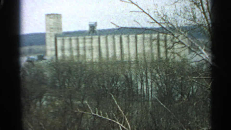 A soft 8mm view of a large Minnesota silo or grain elevator complex beyond bare winter woods.