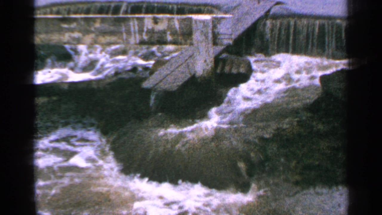 1965 Minnesota 8mm frame showing turbulent whitewater below a concrete dam and spillway structure.