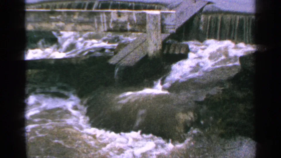 1965 Minnesota 8mm frame showing churning rapids and foamy current near a concrete dam.