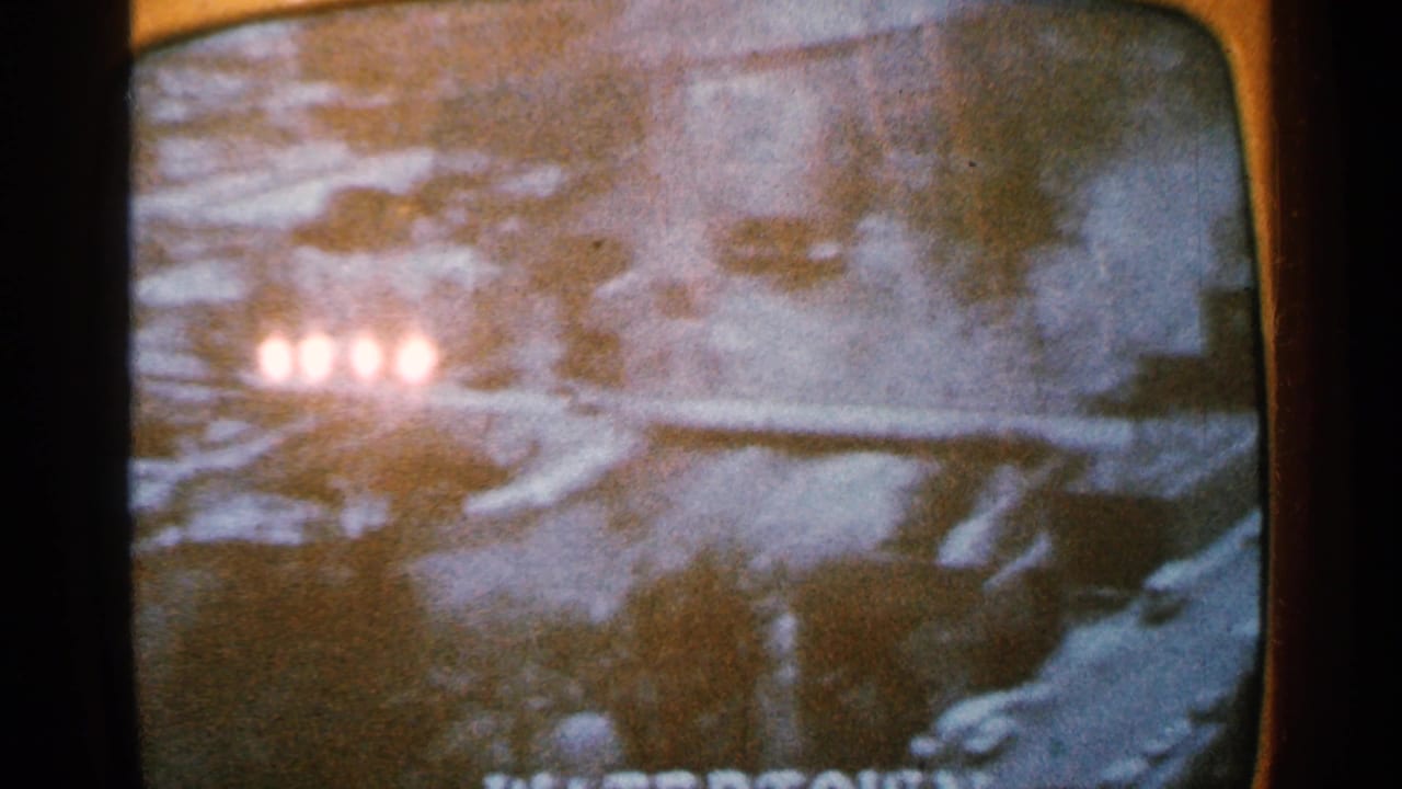 Grainy 1965 8mm frame with four glowing circular lights above a snowy landscape, seen through what appears to be a television or projected screen.