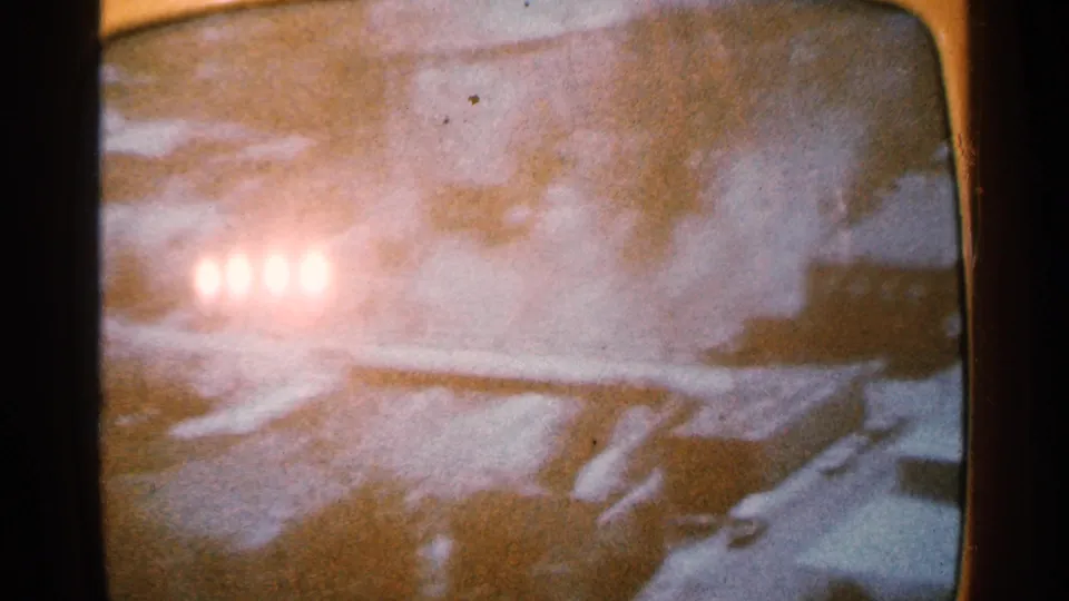 Soft, overexposed 8mm frame showing four bright lights blooming across a snowy screen image, with indistinct dark shapes at the edges.