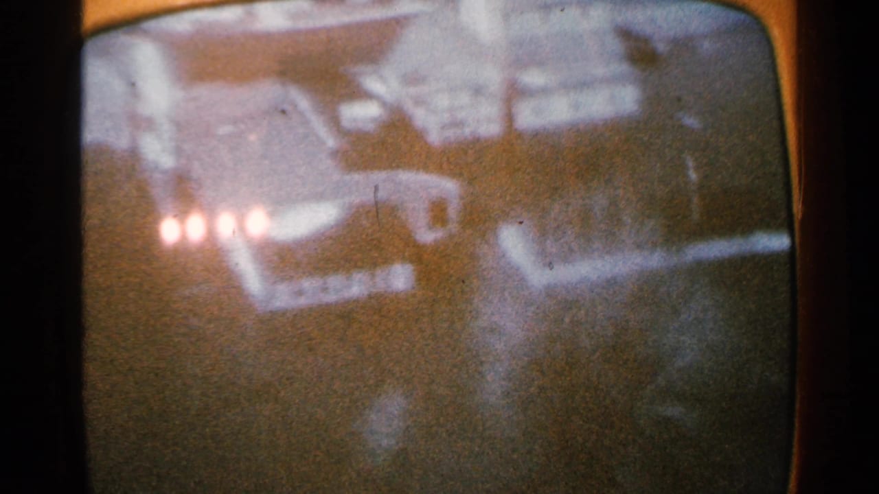 1965 Minnesota home-movie frame showing a soft, grainy snowy scene on a rounded screen with clustered lights and dark forms.