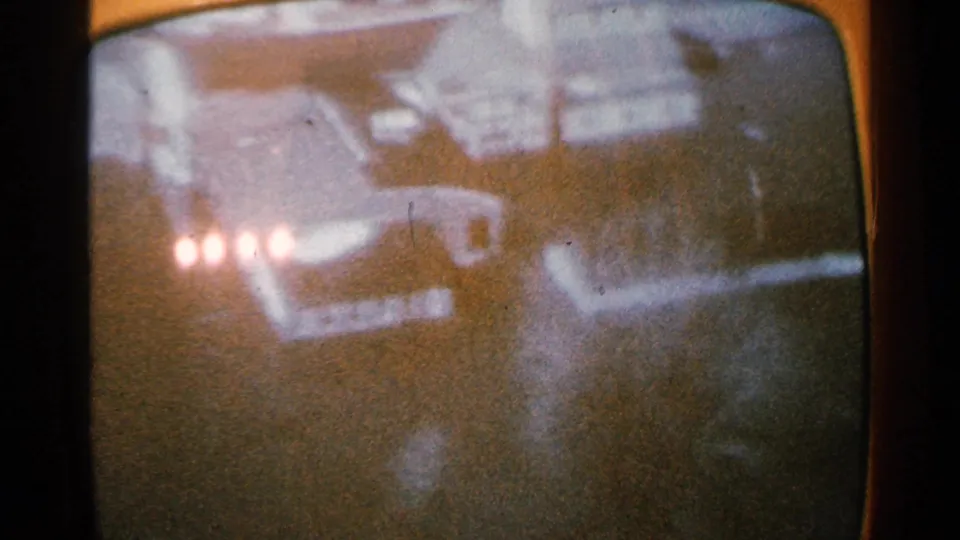 1965 Minnesota home-movie frame showing a soft, grainy snowy scene on a rounded screen with clustered lights and dark forms.