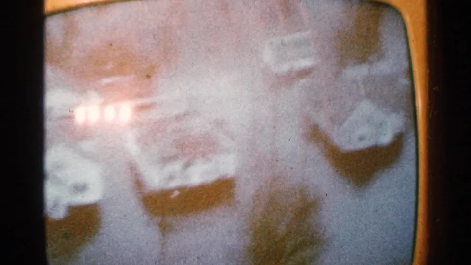 1965 Minnesota flood footage frame with blown-out light flare, pale floodwater, rooftops, and indistinct town structures below.