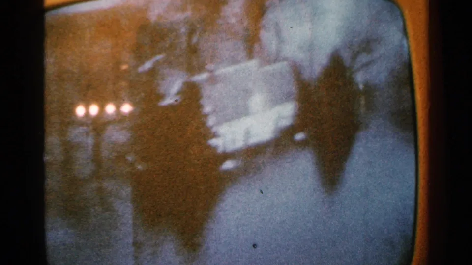 Minnesota 1965 frame with waterlogged ground or street, dark structural silhouettes and small lamps glowing in the distance.