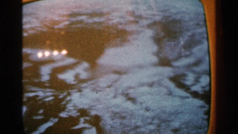 Minnesota 1965 home-movie frame showing murky water, pale debris or snow, and indistinct flood-damaged surroundings.